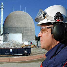 a man wearing headphones and a hard hat stands in front of a large dome at a nuclear facility